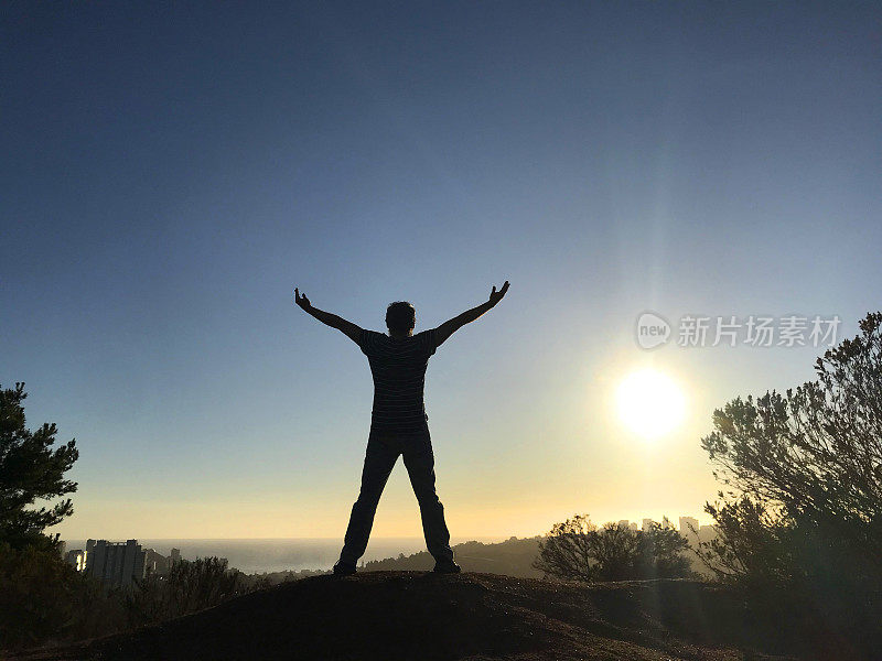 在智利瓦尔帕莱索的维纳(Vina)，一名男子伸开双臂在山顶上庆祝，身后是太平洋的景色和日落，Viña del Mar, Reñaca